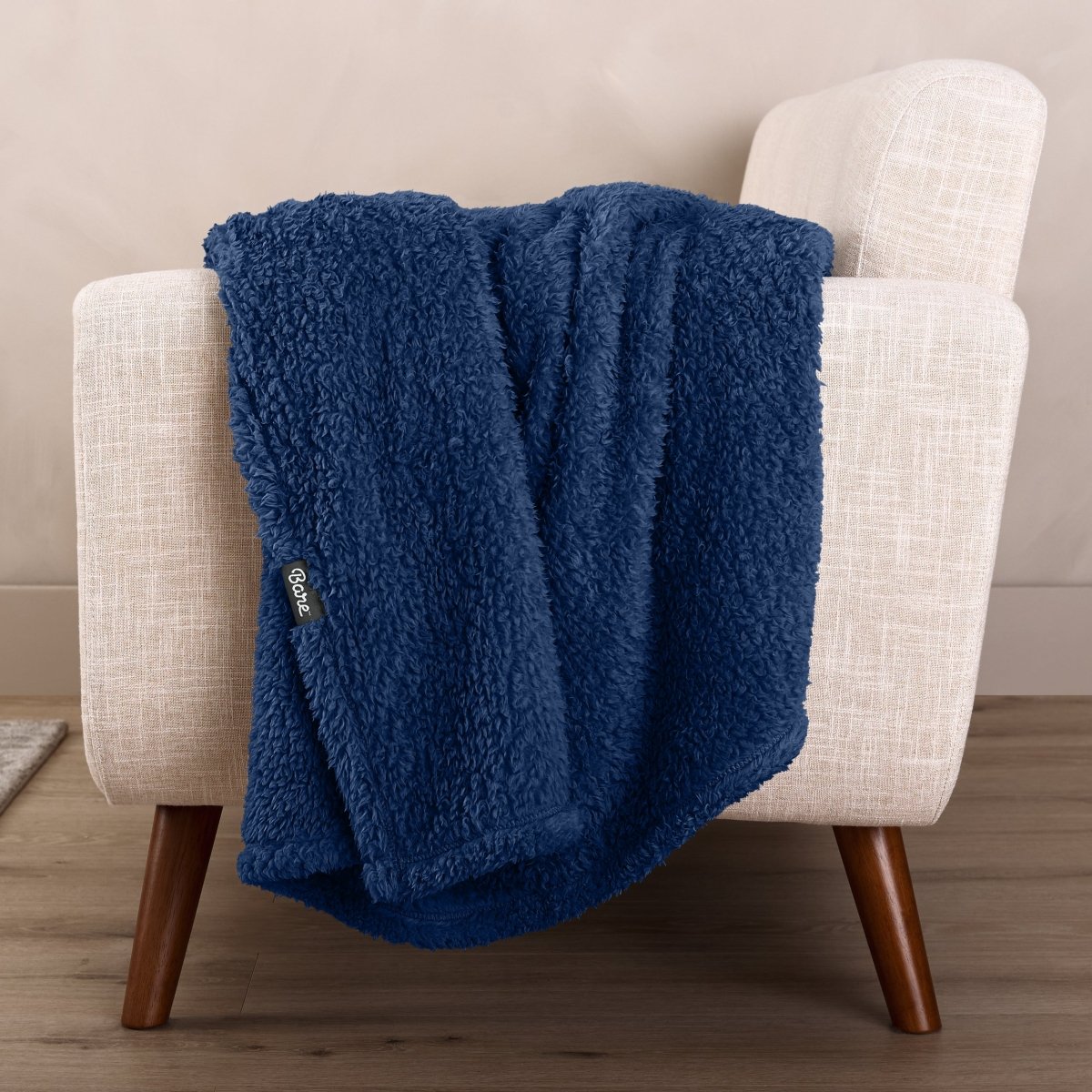 Faux shearling blanket draped over a beige armchair with a wooden base.