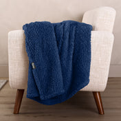 Faux shearling blanket draped over a beige armchair with a wooden base.