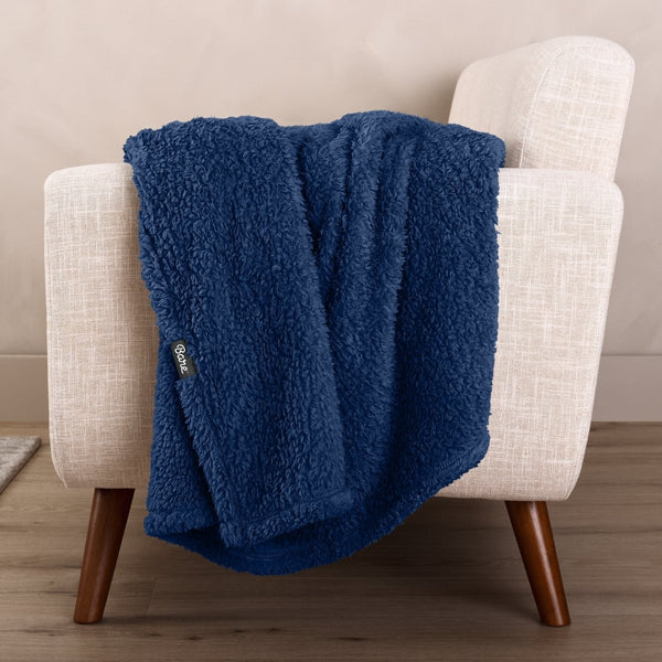 Faux shearling blanket draped over a beige armchair with a wooden base.
