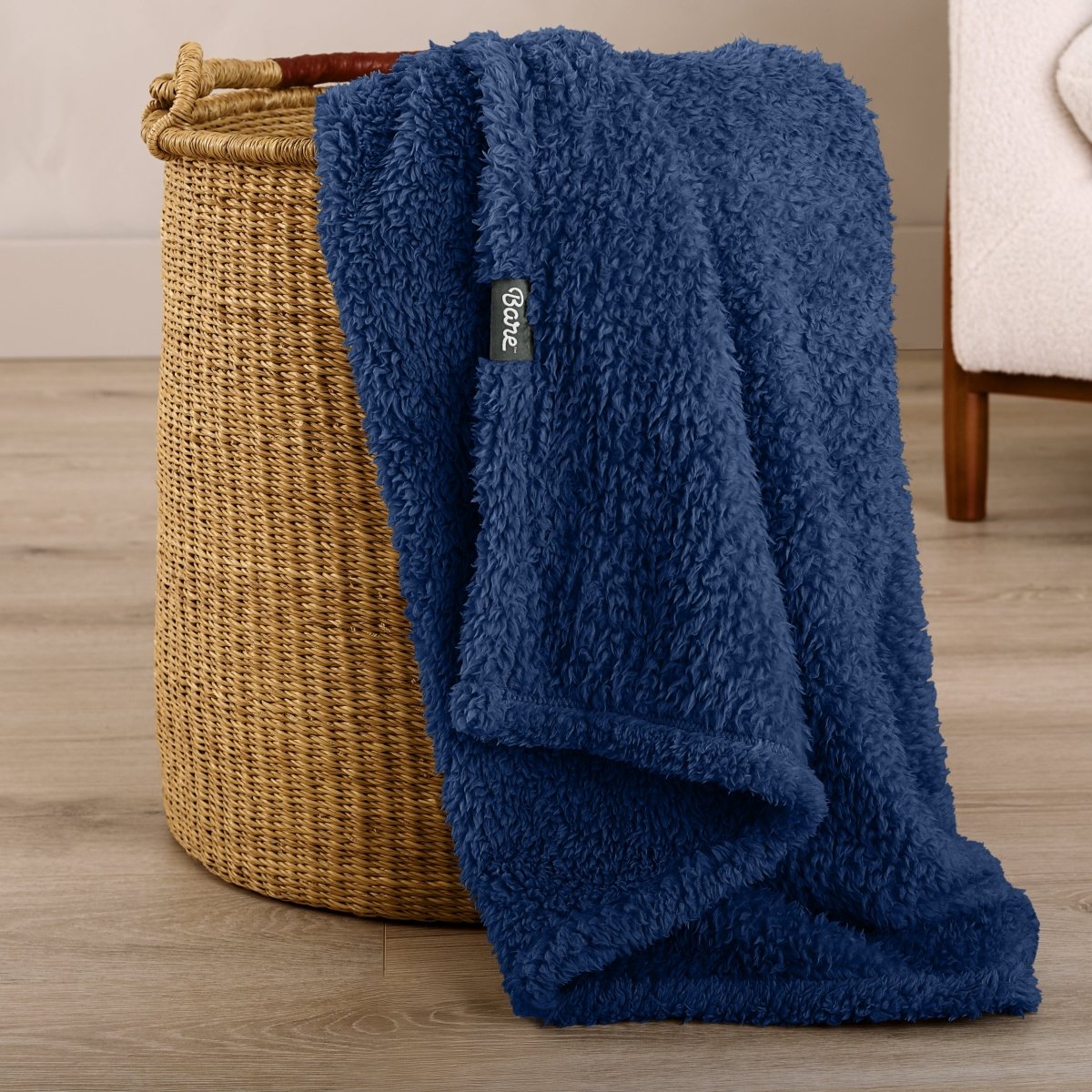 Fluffy blanket draped over a woven basket on a wooden floor.