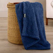Fluffy blanket draped over a woven basket on a wooden floor.
