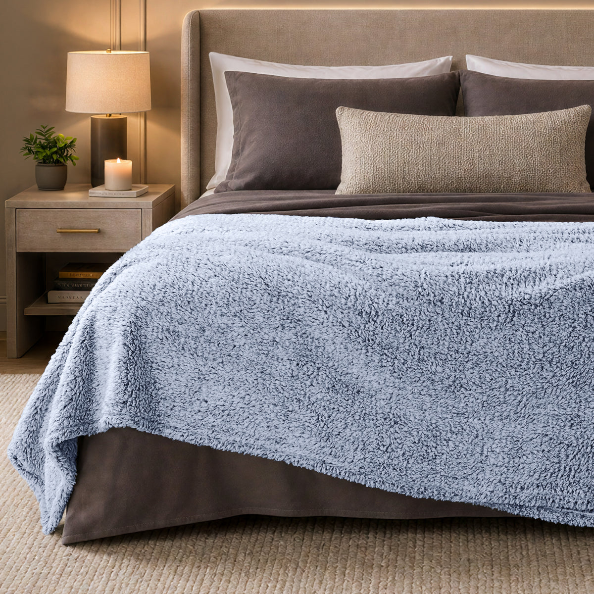 A bed with a tipped sherpa blanket draped over the end