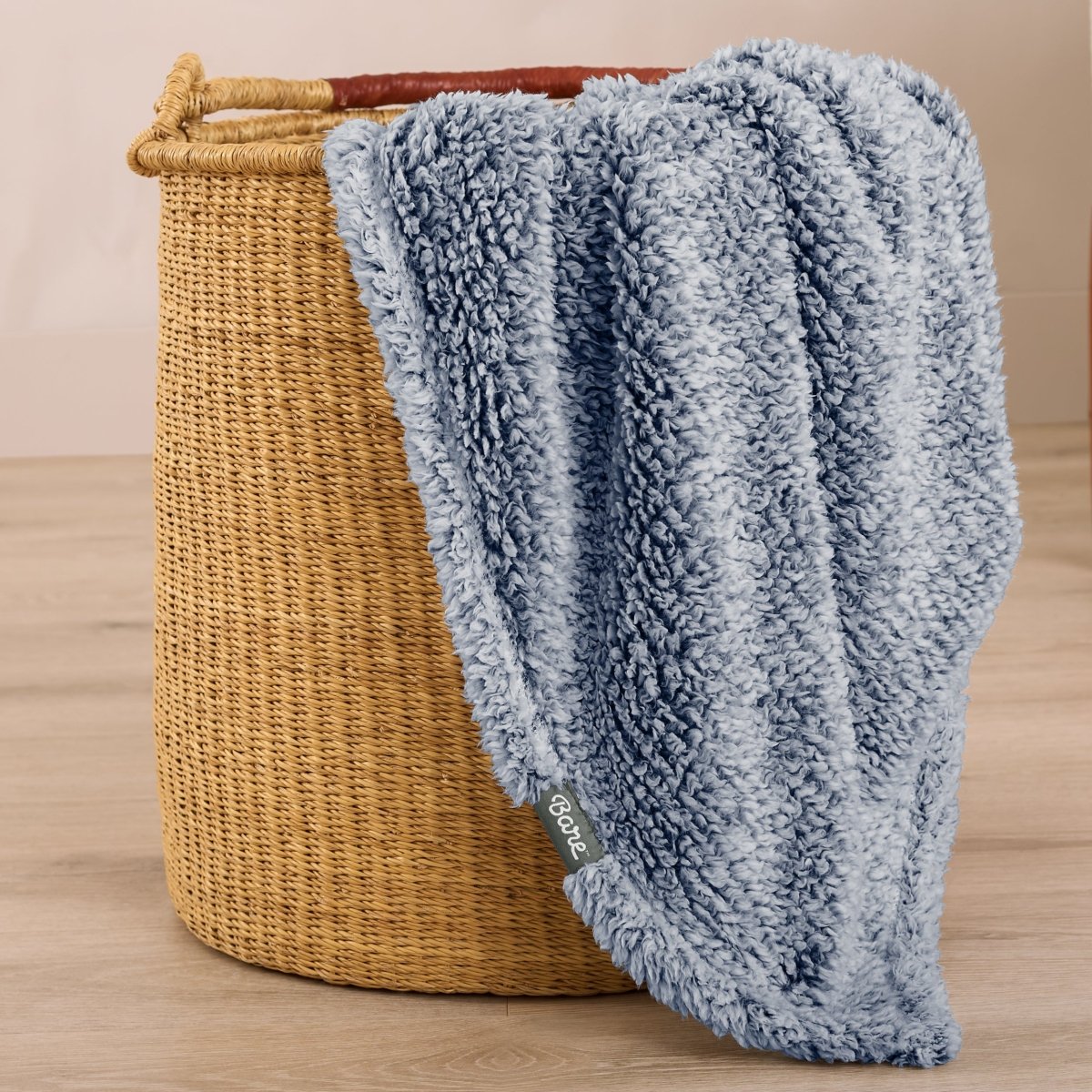 Textured blanket draped over a wicker basket on a wooden surface