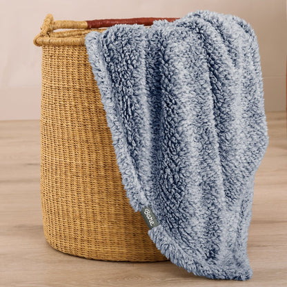 Textured blanket draped over a wicker basket on a wooden surface
