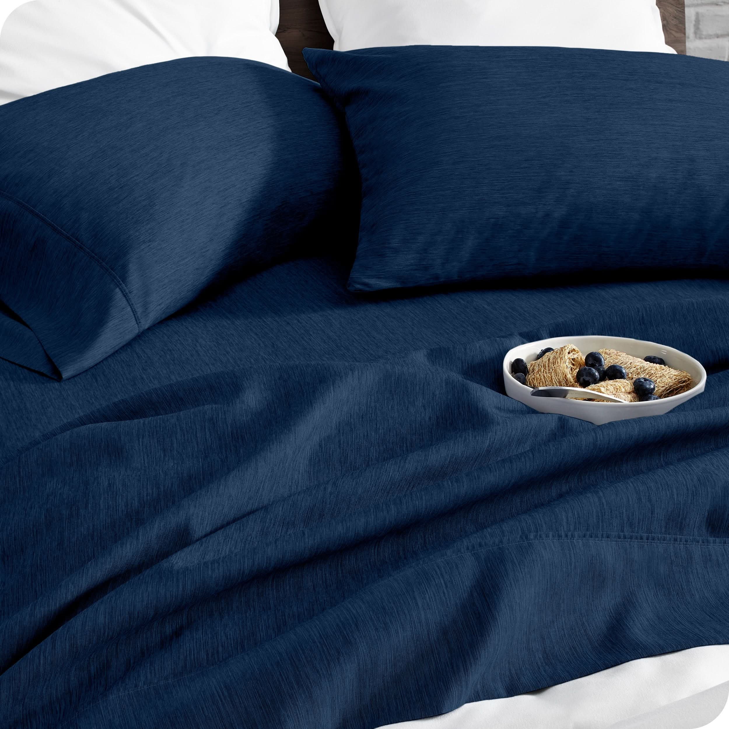 A bed made with sheets. A cereal bowl is on the sheets.