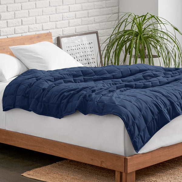 Weighted blanket on a bed with white pillows and a wooden headboard in a room with a plant and brick wall.