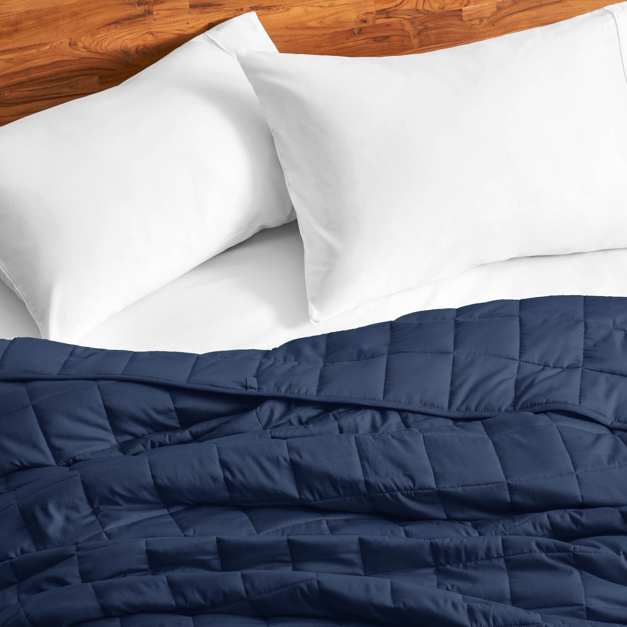 Cotton weighted blanket on a bed with white pillows against a wooden headboard.