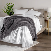 Blanket draped over a bed in a bedroom setting with a nightstand and lamp.