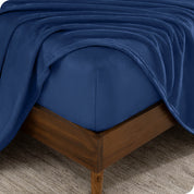The corner of a bed frame and mattress with a fitted sheet and flat sheet on it.