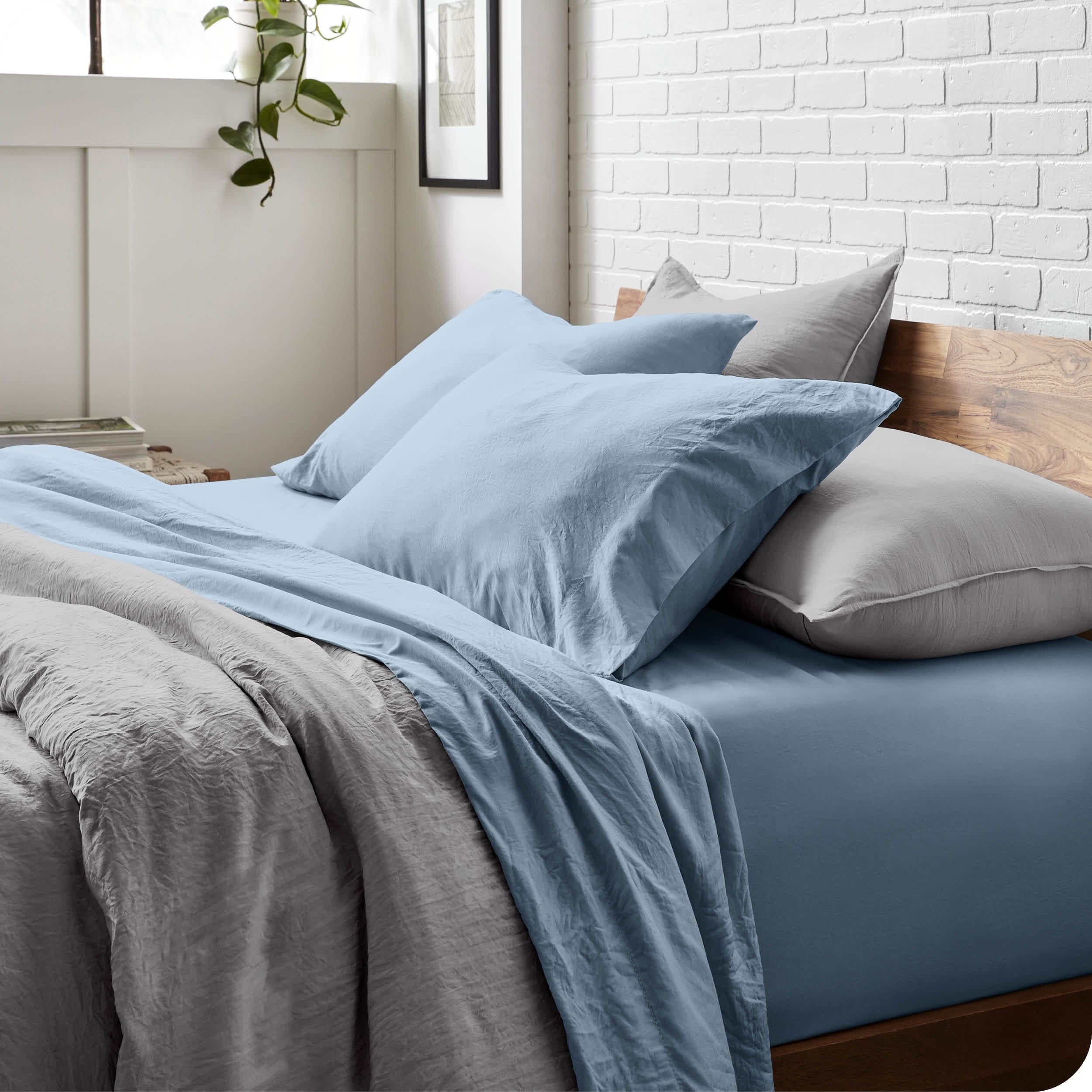 Side view of a bed made with a fitted sheet, pillowcases, and top sheet folded down part way over the duvet cover