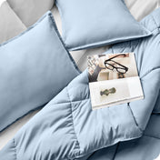 Close up of a comforter set on a bed. There are glasses and a magazine on top of the comforter.