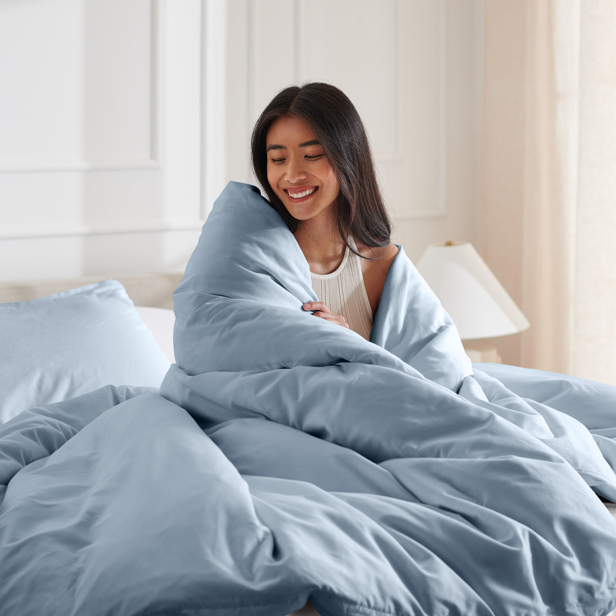 Woman smiling under duvet cover set in a bedroom setting