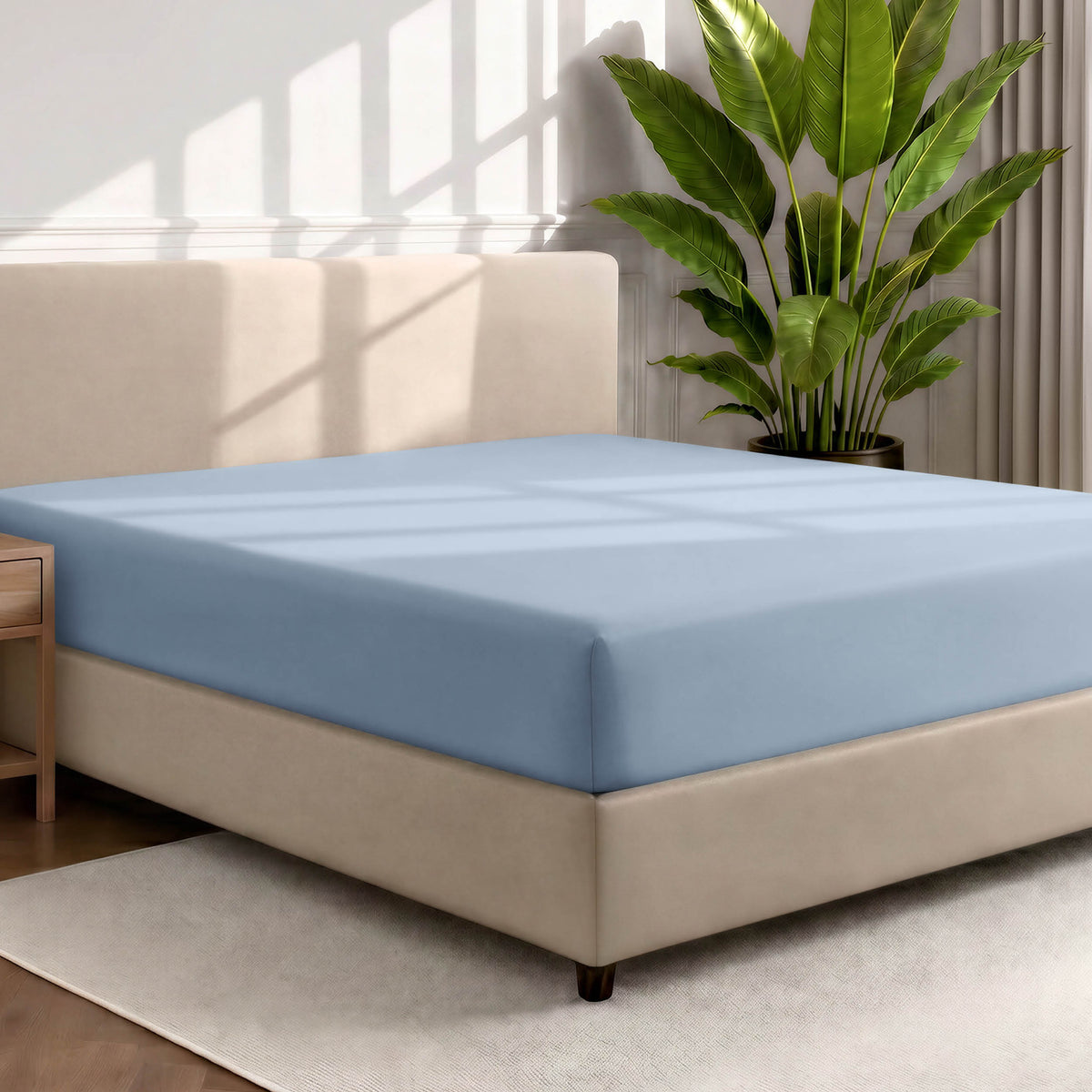 Bed with a fitted sheet in a room with a large plant and rug