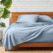 A wooden bed frame with a microfiber sheet set on the mattress.