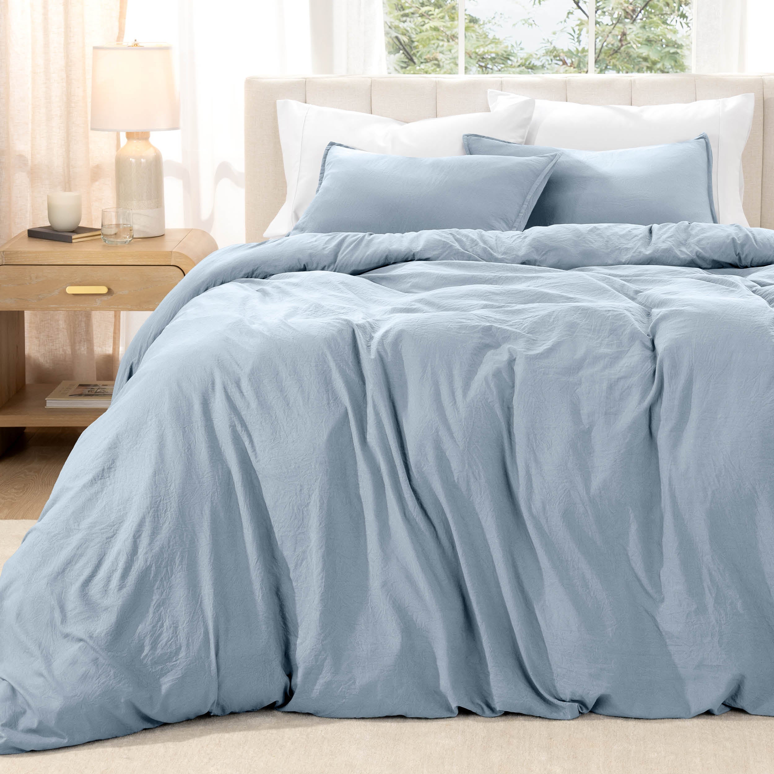 Bed with washed bedding and white pillows in a bright room
