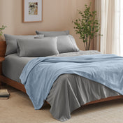 A bed made with grey sheets and a microplush blanket