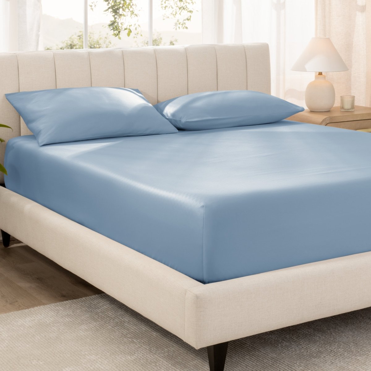 Bed with fitted sheet and pillowcases in a bright room.