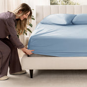 Woman adjusting a fitted sheet on a bed in a bedroom setting