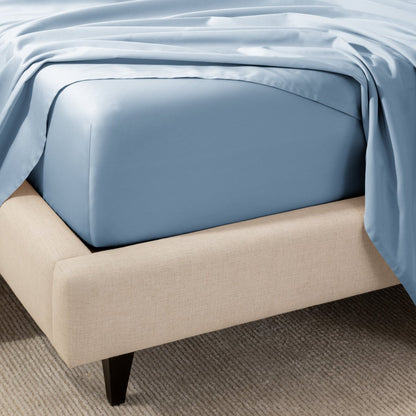 A close-up of the corner of a bed with a fitted sheet and matching flat sheet.