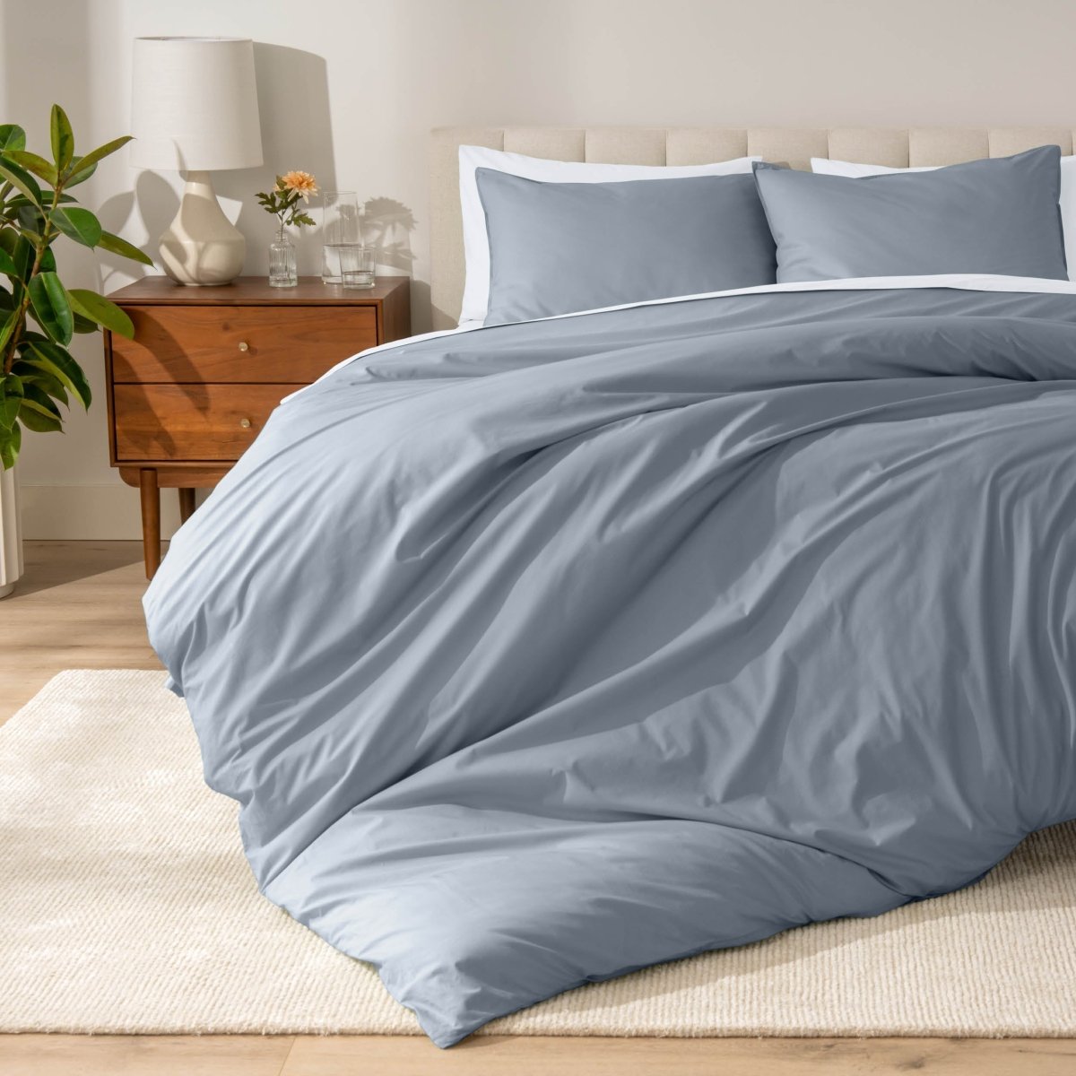 Percale bedding set on a bed in a bedroom with a wooden nightstand and lamp.