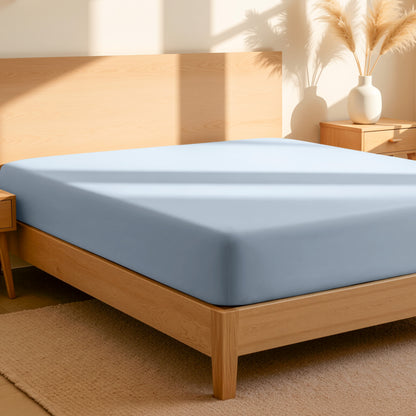 Fitted sheet on a bed in a bedroom setting with a lamp and plant.