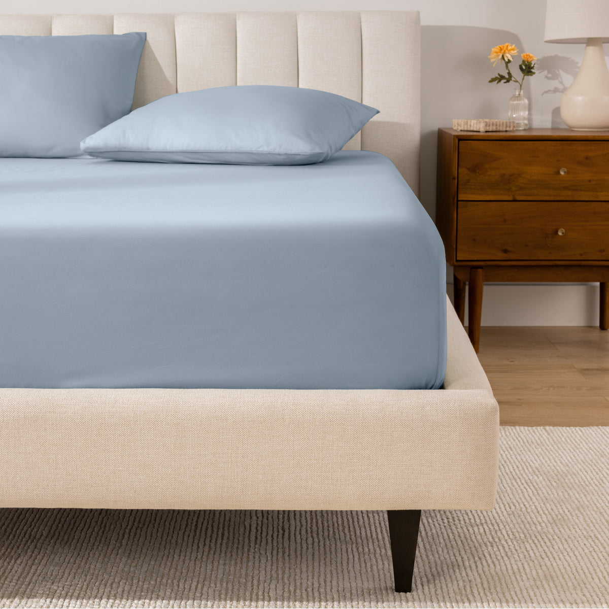 A percale fitted sheet and pillowcases on a bed in a bedroom with a wooden nightstand.