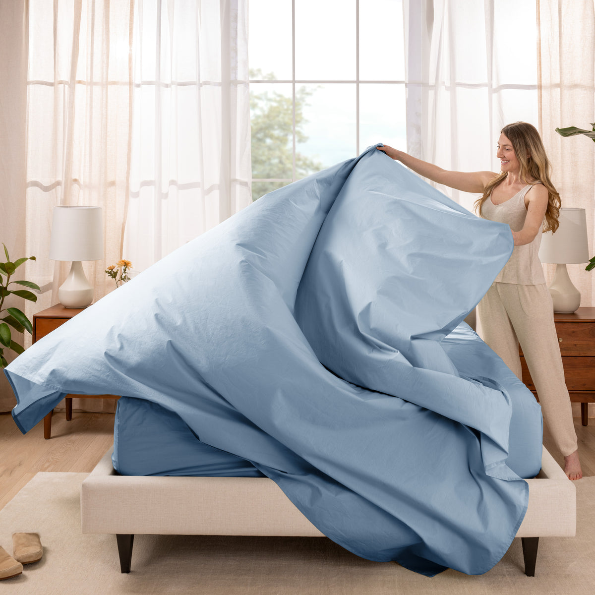 Woman putting a sheet set on a bed in a bright bedroom.