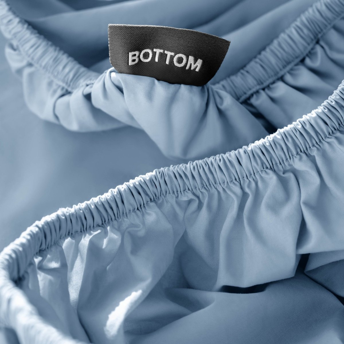 Close-up of a fitted sheet with a black fabric brand label reading BOTTOM.