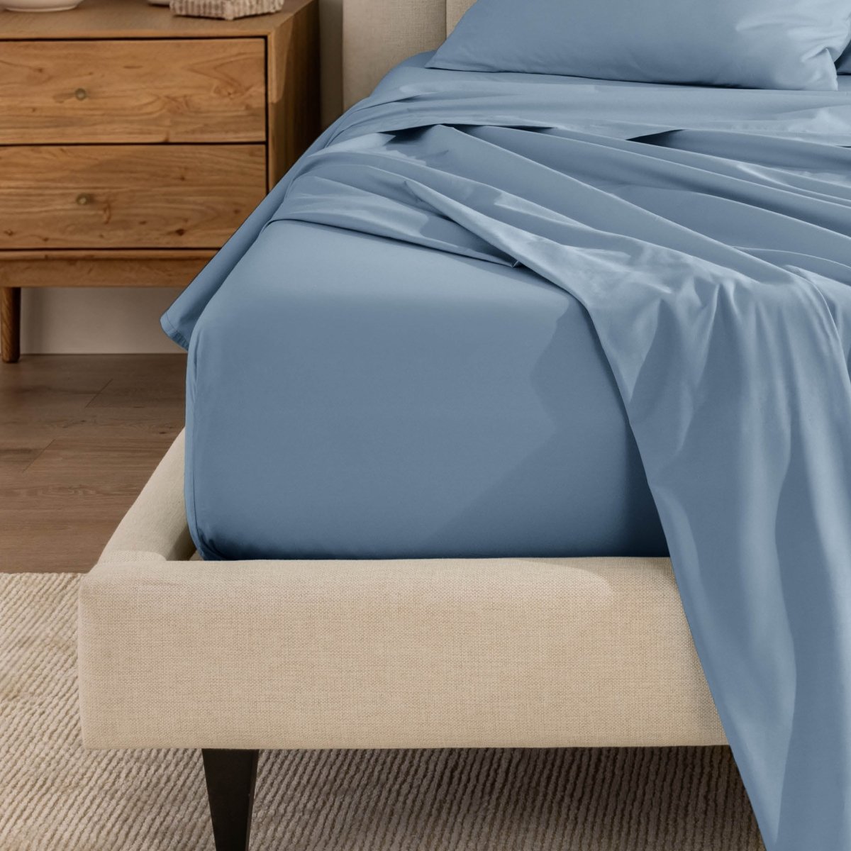 Top sheet and a matching fitted sheet on a bed with a beige bed frame