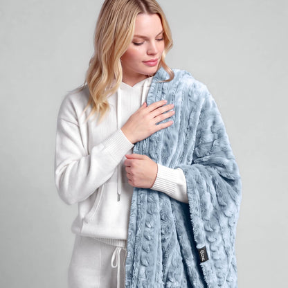 A woman is standing with a textured faux shearling blanket over her shoulder