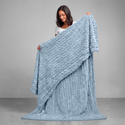 A woman is standing and holding a textured cable knit blanket