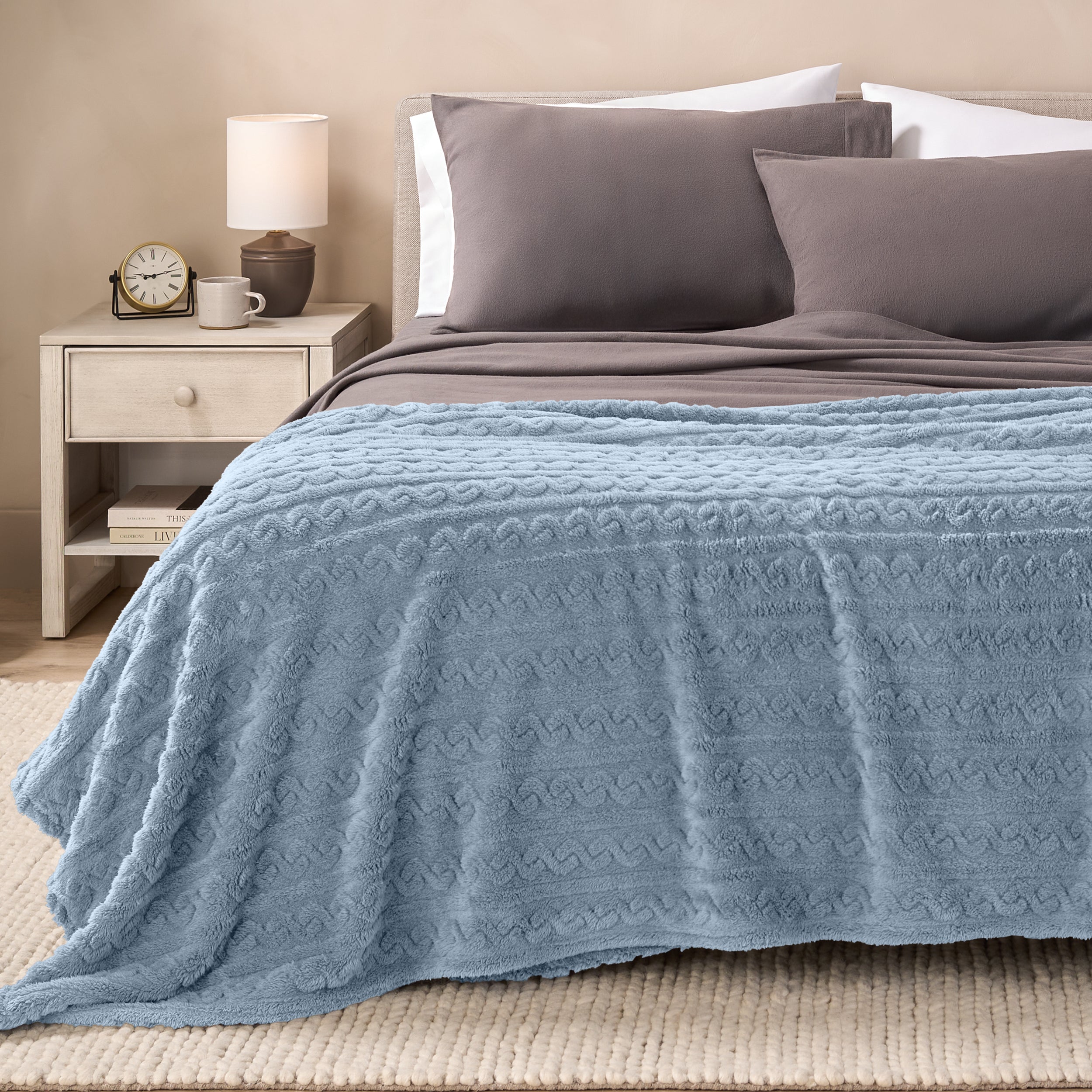 A textured sherpa blanket draped over the end and side of a bed