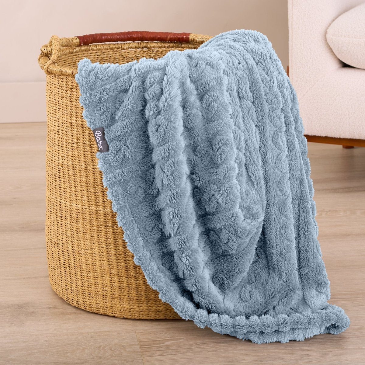 Blue textured blanket draped over a woven basket on a wooden floor.