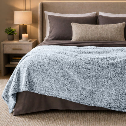 A bed with a tipped sherpa blanket draped over the end