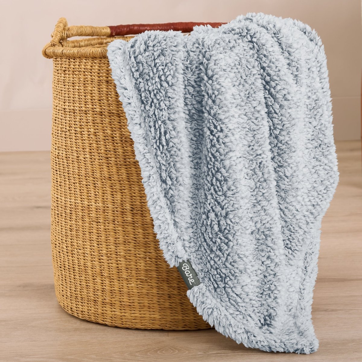Textured blanket draped over a wicker basket on a wooden surface