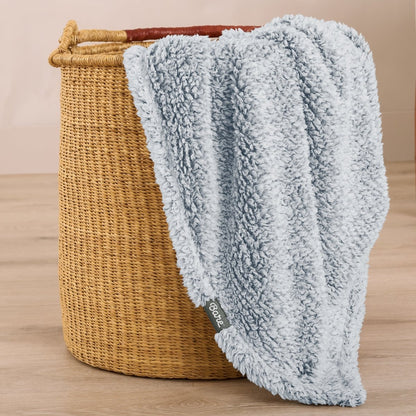 Textured blanket draped over a wicker basket on a wooden surface