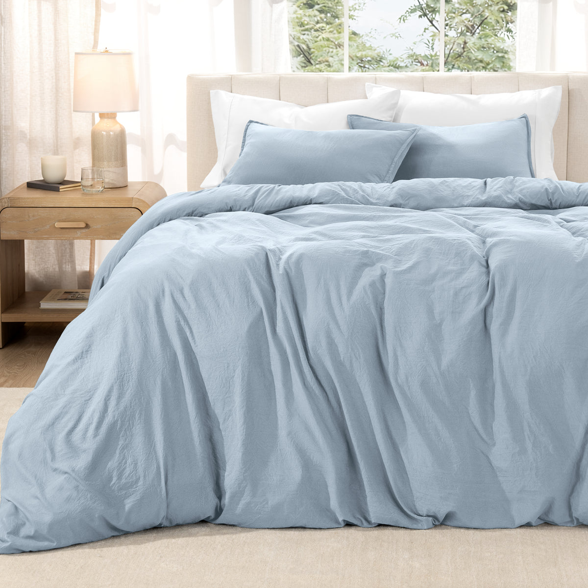 Washed duvet set on a bed in a bright bedroom with a lamp and window.