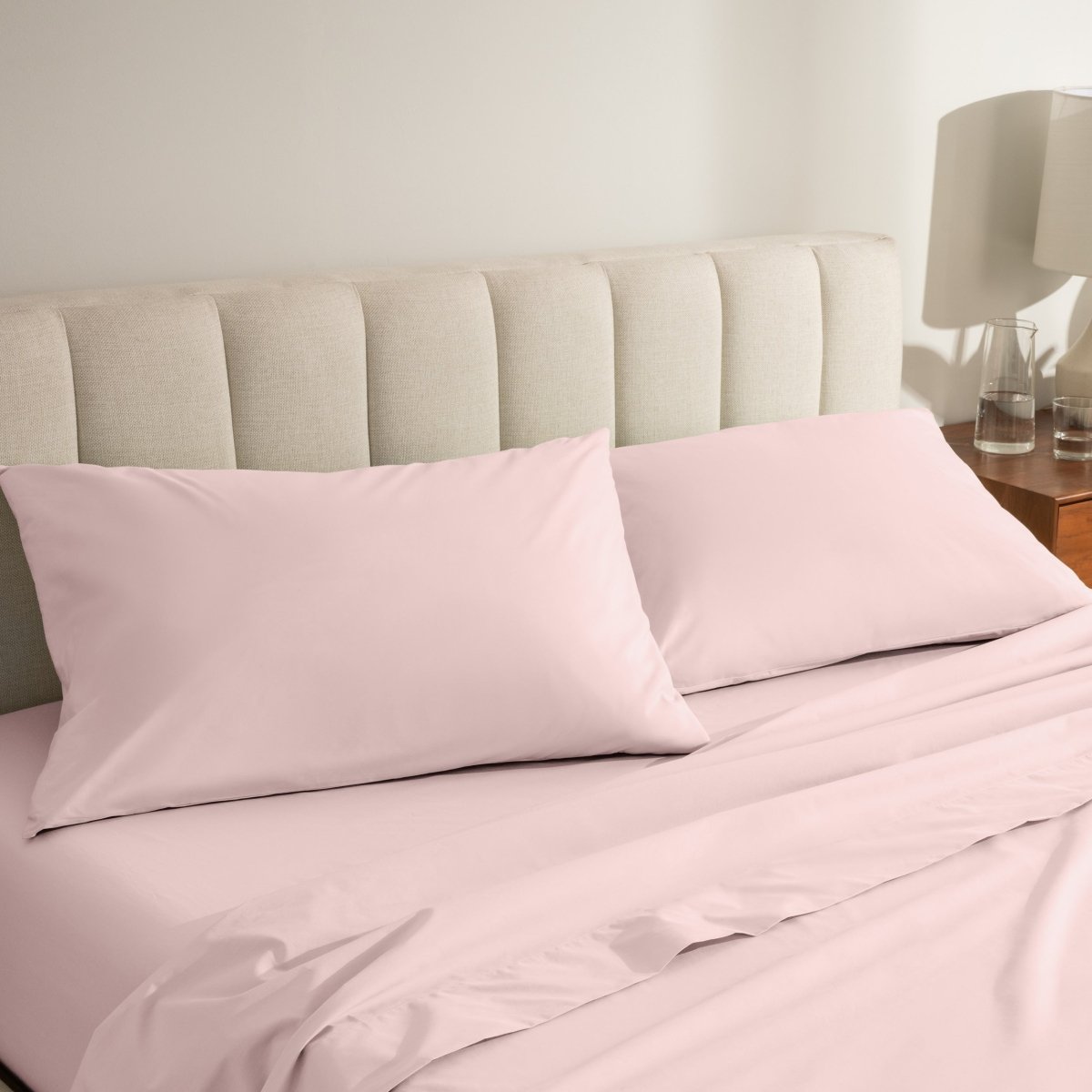 Percale bed sheets and pillowcases on a neatly made bed with a beige headboard.