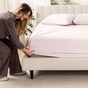 Woman adjusting a fitted sheet on a bed in a bedroom setting