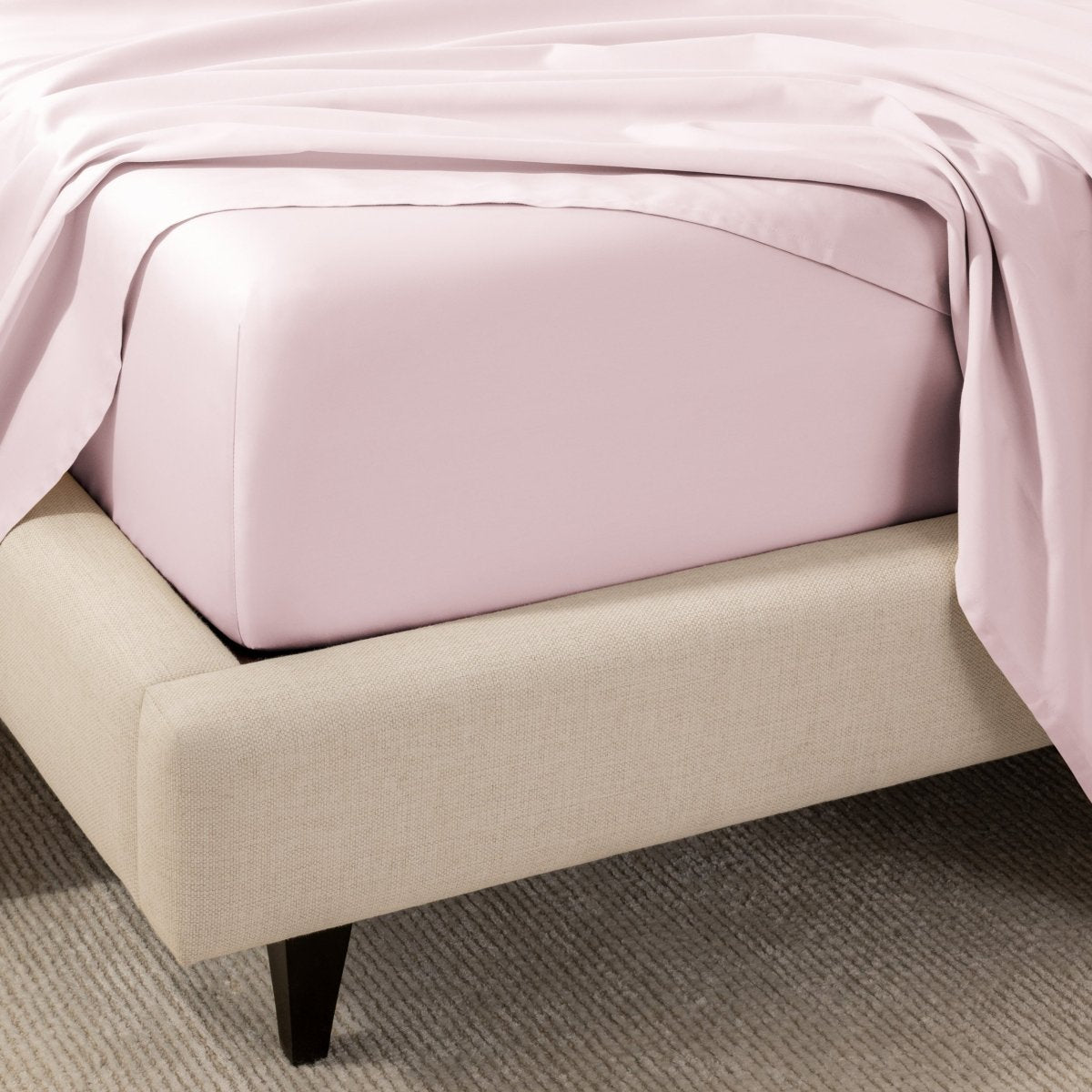 A close-up of the corner of a bed with a fitted sheet and matching flat sheet.
