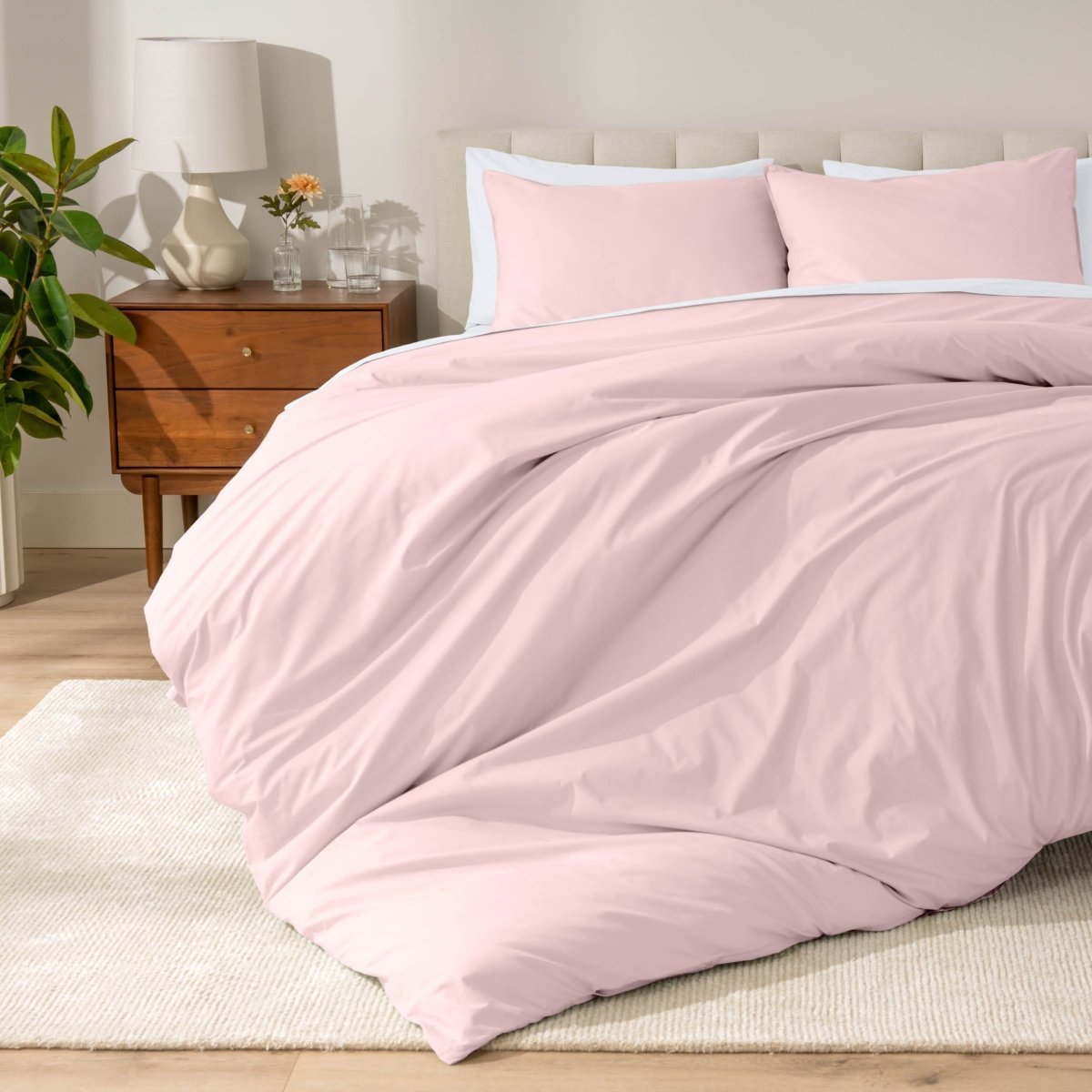 Percale bedding set on a bed in a bedroom with a wooden nightstand and lamp.