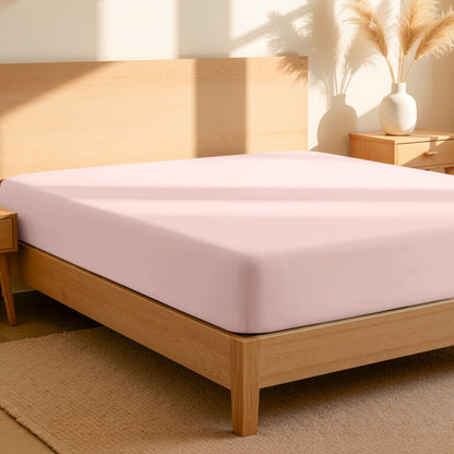 Fitted sheet on a bed in a bedroom setting with a lamp and plant.