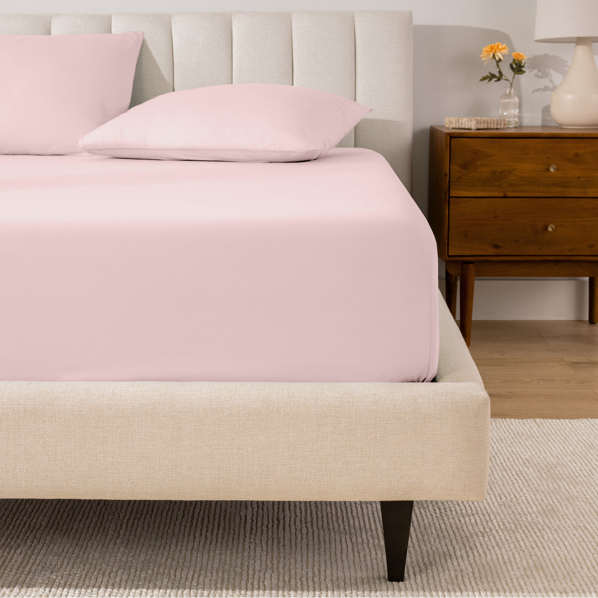 A percale fitted sheet and pillowcases on a bed in a bedroom with a wooden nightstand.