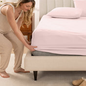 Woman in pajamas adjusting bed sheets on a bed.