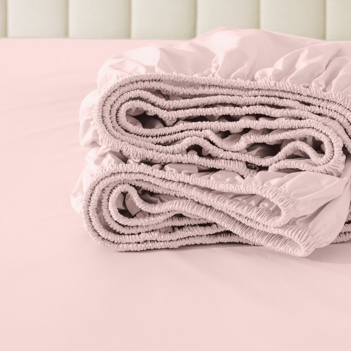 Folded fitted sheet on a bed with a neutral background