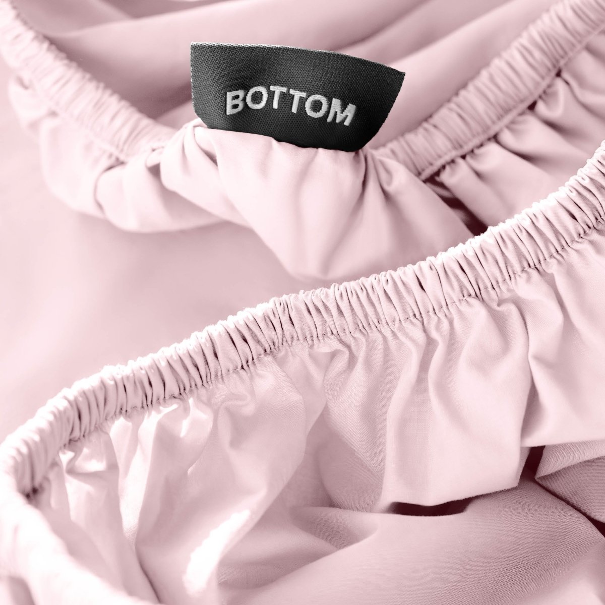 Close-up of a fitted sheet with a black fabric brand label reading BOTTOM.