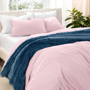 Washed bedding set on a bed in a bedroom with plants and nightstands.