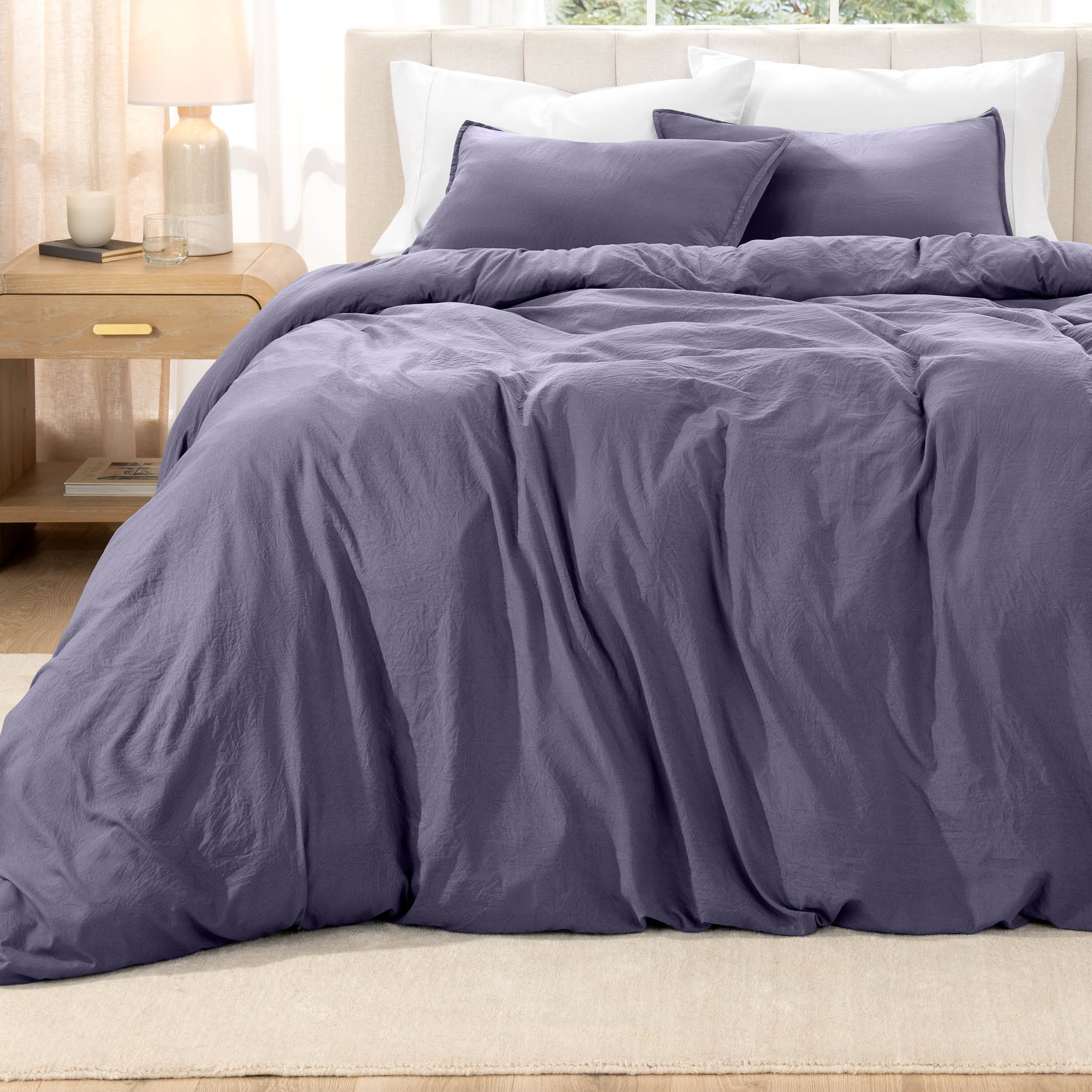 Bed with washed bedding and white pillows in a bright room