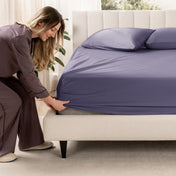 Woman adjusting a fitted sheet on a bed in a bedroom setting
