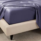 A close-up of the corner of a bed with a fitted sheet and matching flat sheet.